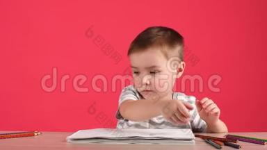 可爱的小男孩用铅笔在粉红色背景的<strong>相册</strong>里画画。
